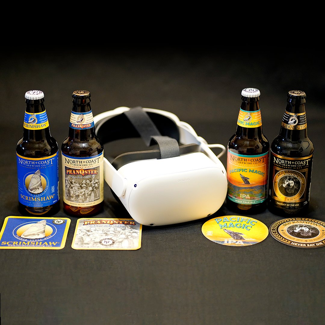A white virtual reality headset sits in the middle of the photo with a grey background. To the left of the headset are two beer bottles and two beer coasters. To the right of the headset are two more beer bottles and two coasters.