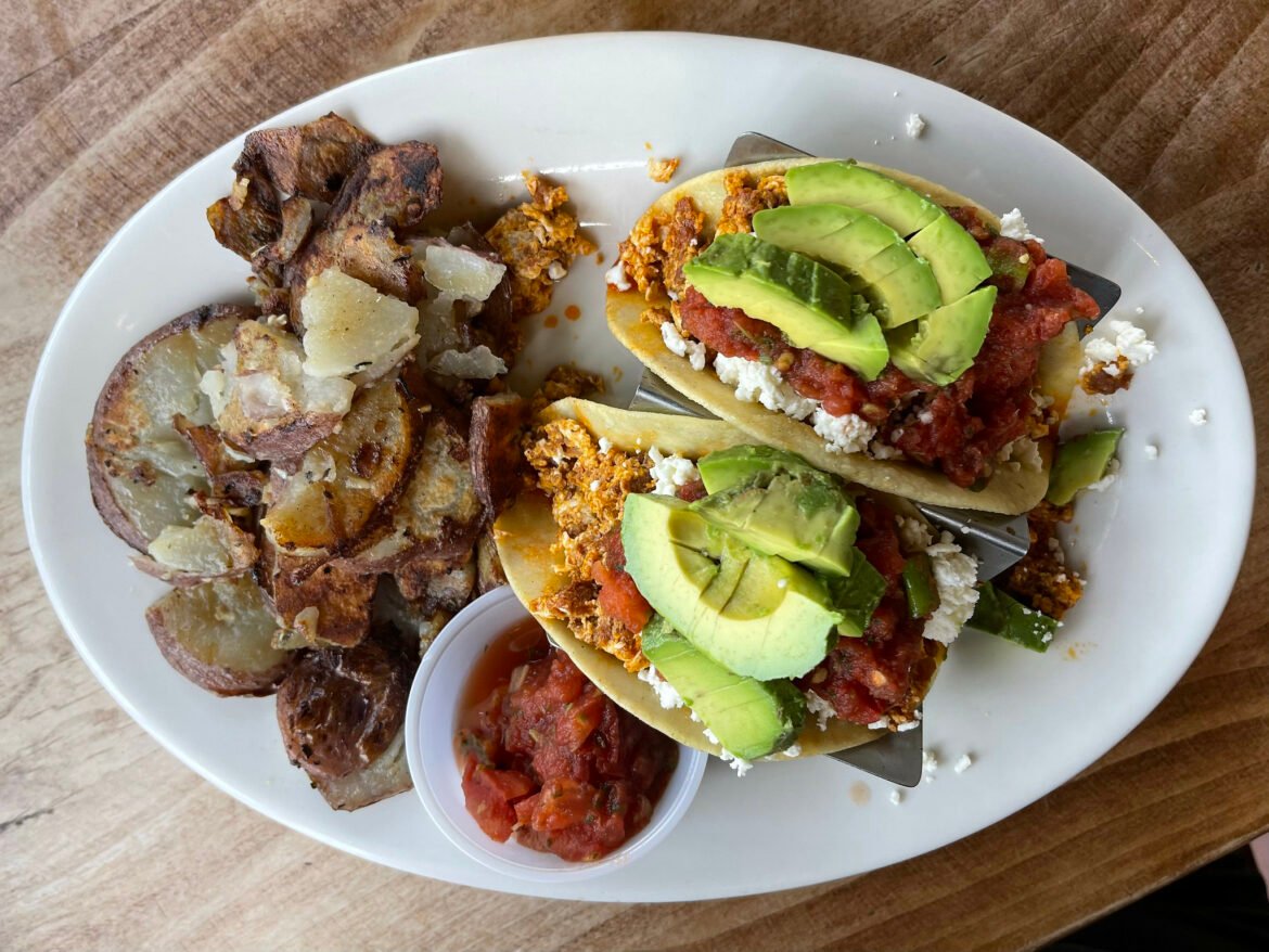 A plate with fried breakfast potatoes, a cup of salsa, and two breakfast tacos with chorizo, salsa and avocado.