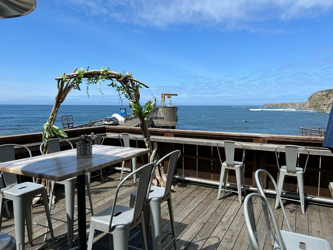 A wooden patio with metal chairs and tables overlooking the ocean.